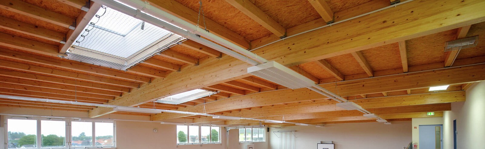 Sporthalle der Ganztagsschule Rostock: Holzbalkendecke mit Oberlichtern über dem Hallenfeld